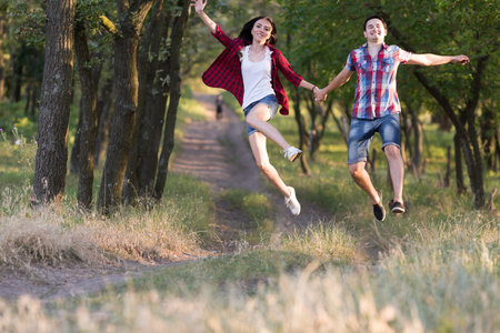 Girl and Guy running jumping holding Hands on Forest Trailの写真素材