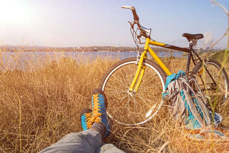 Person in bright sporty Shoes resting on Grass along Bicycleの写真素材