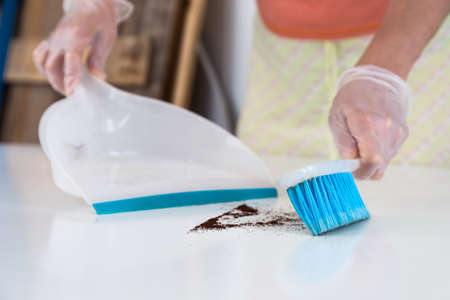Woman cleaning garbage from white table with Brush and Shovelの写真素材
