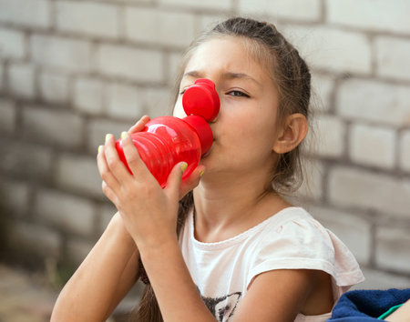 Little baby girl drinking water of red plastic flaskの写真素材