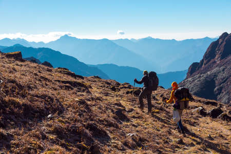 Hikers with Backpacks walking on grassy heel in Mountainsの写真素材