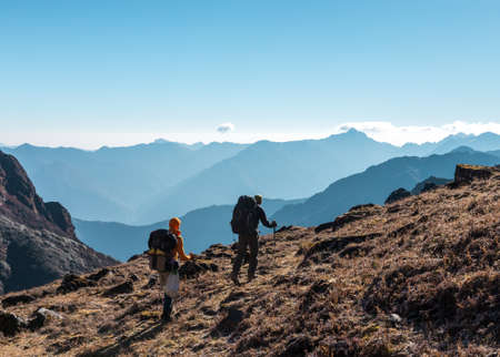 Two Hikers with Backpacks walking on grassy heel in Mountainsの写真素材