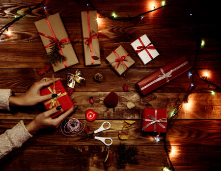 Hands of female carefully preparing many gifts with Christmas lightsの写真素材
