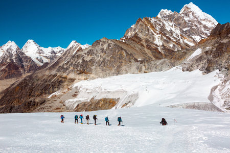 Iconic View of high Altitude Himalaya Mountains and group of Climbers walking up on snowy Glacierの写真素材