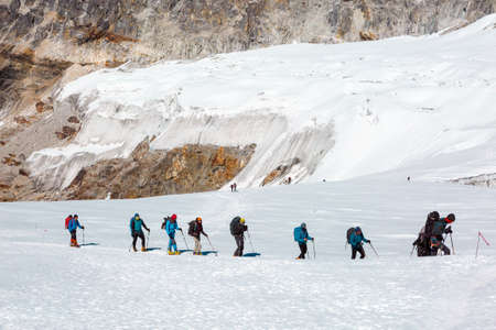 Mountain Climbers walking on snowy Glacier among high Peaksの写真素材