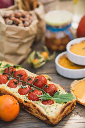 Pie with cherry tomatoes, pumpkin pie, orange and paper bag with nuts on a wooden tableの写真素材