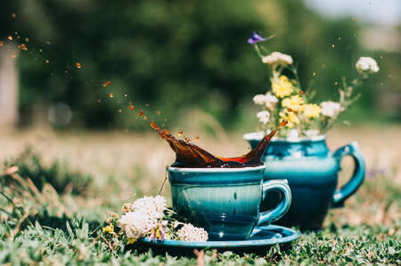 blue ceramic cups with a milkman on the grass with a splash of coffee decorated with summer flowersの写真素材