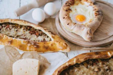 Adzharian khachapuri with egg and traditional turkish pide with meat and piece of cheese on a white wooden tableの写真素材
