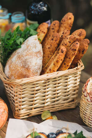 Wicker basket with bread, ciabatta, greens and arugula on a wooden table. Autumn picnicの写真素材