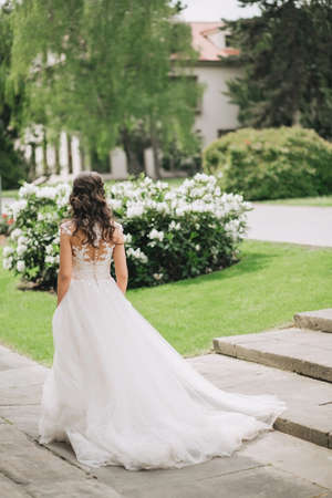 The delicate beautiful bride walks in the park in a wedding dress with lace and plume, bush with flowers. Fine artの写真素材