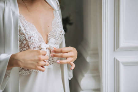Girl bride tenderly touching bow, dressed in white lace and silk dressing gown in the wedding morningの写真素材