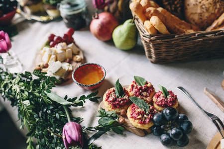 Snack from crackers and beets, grapes, honey, cheese. Wicker basket with bread on the table decorated with flowers and boxwoodの写真素材