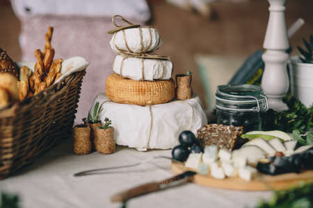 A pile of cheese heads in a paper, next a sliced cheese, a basket of bread and grapes, wine and plant plugsの写真素材