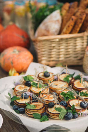 Canape of pancakes with blueberries, wicker basket with bread and pumpkinの写真素材