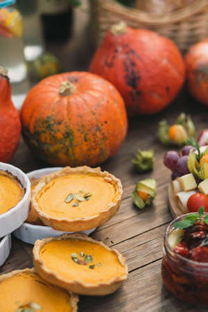 Beautiful pumpkin pies lying next to pumpkins, dried tomatoes and physalis on a wooden tableの写真素材