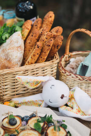 Wicker basket with bread, ciabatta, toy bunny and arugula on a wooden table. Autumn picnicの写真素材