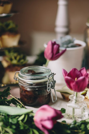 Glass jar with olives next to pink tulips and a white pot