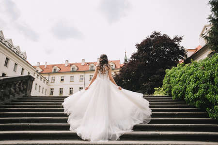 Happy beautiful bride outdoors. The bride in a beautiful fluttering wedding dress on the stairs against the background of the European houseの写真素材