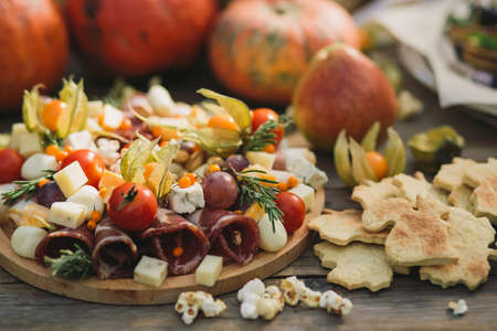 Meat cut, ham, cheeseboard, cheese, physalis, popcorn next to figured cookies and pumpkins at a picnicの写真素材