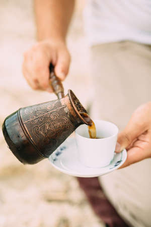 A man pours turkish coffee from a metal coffee pot into a white cup and saucer. Verticalの写真素材