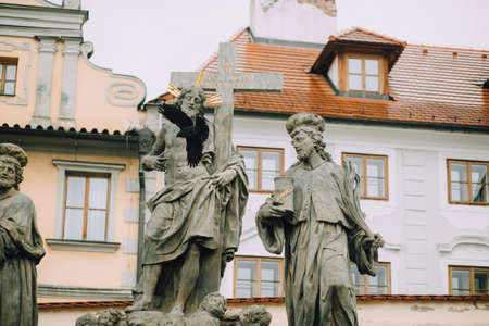 Prague, Czech Republic - May 2014. Sculpture of the Holy Savior with Cosmas and Damian, the holy healers on the Charles Bridge on the background of red roofs and a flying black crow.のeditorial素材