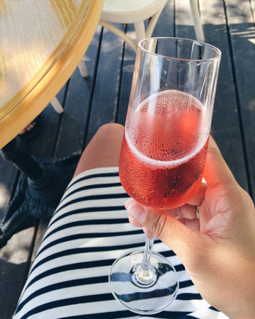Sweaty glass with red champagne in hand against the background of legs and striped dressの写真素材