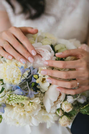 A beautiful gentle beige manicure of the elegance bride in her arms. Hands on a white wedding bouquet. Close upの写真素材