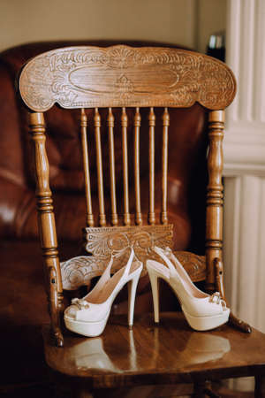 A pair of beautiful white wedding shoes with high heels stand on a wooden vintage chair. Verticalの写真素材
