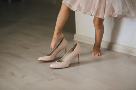 A little girl in a dress wearing foot adult mum's high-heeled shoes.の写真素材