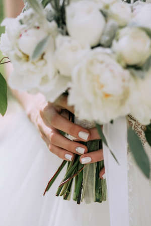 Beautiful elegant wedding bouquet of white peonies in the hands of the bride with a stylish manicure. Close upの写真素材