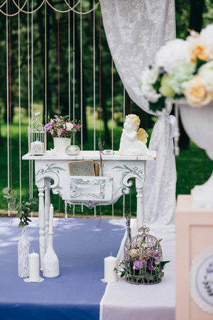 Decorative white vintage table at the wedding ceremony, candle-decorated books with flowers and ceramic angles and a cage on the purple carpet. Verticalの写真素材