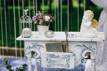 Decorative white vintage table at the wedding ceremony, candle-decorated books with flowers and ceramic angles and lavender. Horizontalの写真素材