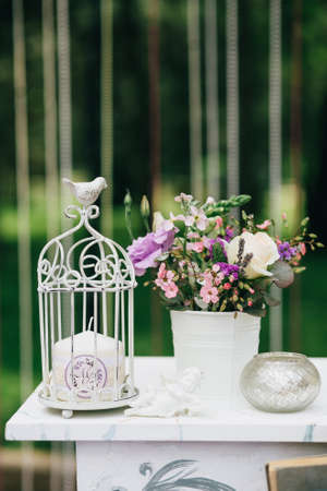 Decorative white vintage table for the wedding ceremony, decorated with a candle in a cage with a bouquet of flowers from roses in the style of Provenceの写真素材