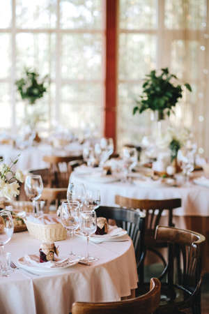 Decorated wedding table in rustic style for dinner with white and beige tablecloths, wine glasses for flowers and Viennese wooden chairs. Verticalの写真素材