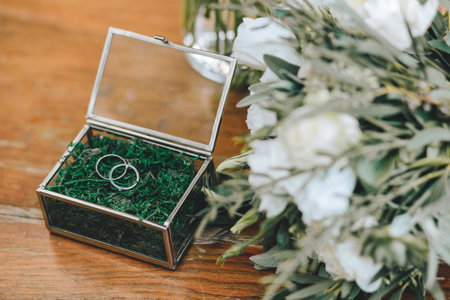A beautiful glass box for wedding gold rings with moss. Near a bouquet of a bride with white flowers on a wooden backgroundの写真素材