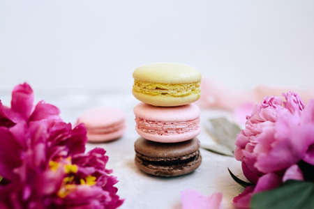 A pile of colorful delicious macaroon closeup with pink peony flowers on a light background. Horizontalの写真素材