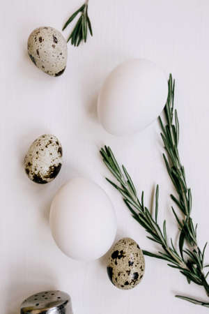 White chicken and quail eggs and a branch of rosemary on a white wooden background. Verticalの写真素材