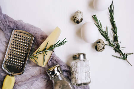 Flatlay Composition. Parmesan hard cheese with rosemary, glass saltcellar and pepper, white chicken eggs and quail, grater and purple gauze fabric on a backgroundの写真素材