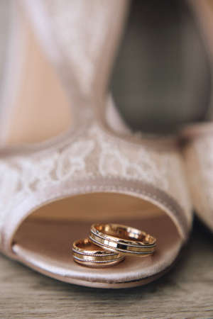 Gold wedding rings with a design are on the brides shoes with a lace. Close up. Verticalの写真素材
