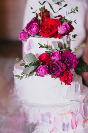 Multi tiered beautiful wedding cake with white cream decorated with pink and red roses and eucalyptus. Verticalの写真素材