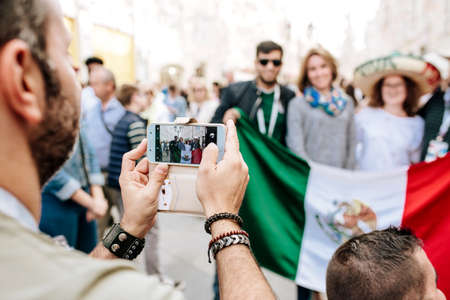 MOSCOW, RUSSIA - JUNE 2018 Hands of a man with a phone close-up, he is photographed by fans of Mexico with the flag of the country in a sombrero in the center of Moscow during the World Cupのeditorial素材