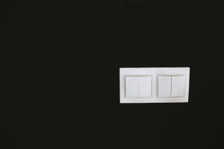 Double white light switches on a black wall background. Horizontalの写真素材