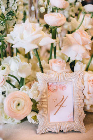 Flower arrangement of white roses and a beautiful frame with the number four, the numbering of the table at the banquet. Verticalの写真素材