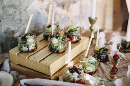 A beautiful decorated buffet table at a party with snacks in glass jars on a wooden box and canapes. Horizontal.の写真素材