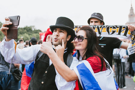 MOSCOW, RUSSIA - JULY 2018 A man in a kettle hat, bow tie and suit asks a girl to kiss with the Russian flag in the fan zone during the World Cupのeditorial素材
