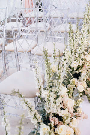 A number of transparent designer chairs at the wedding ceremony alongside beautiful floral arrangements of roses and buttercups. Verticalの写真素材