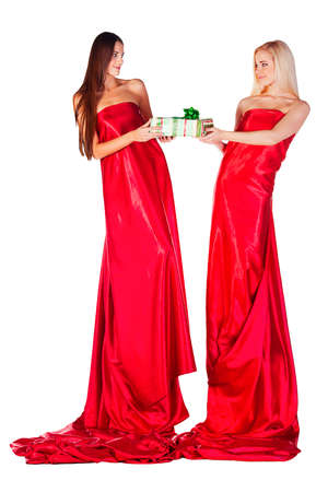 two women in red dress with present in hands looking to each other on white backgroundの写真素材