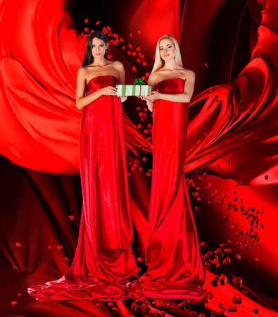 two women in red dress with present in hands on red draperyの写真素材