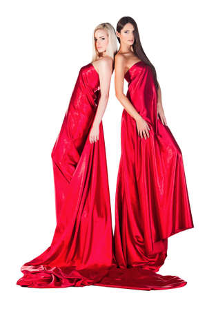 two women in long red dresses standing back to back on white backgroundの写真素材