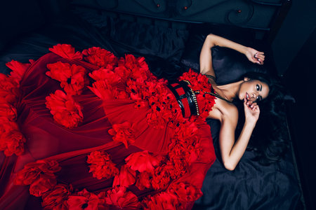 brunette woman in red dress on bedの写真素材